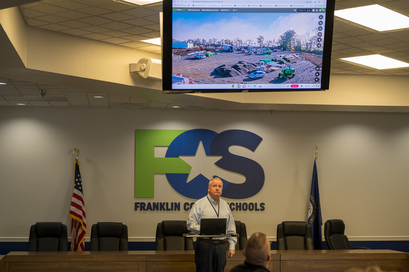 Superintendent Mark Kopp presenting to facility updates to group. FCS logo in background. USA and KY flags present too. TV with update on EES construction.