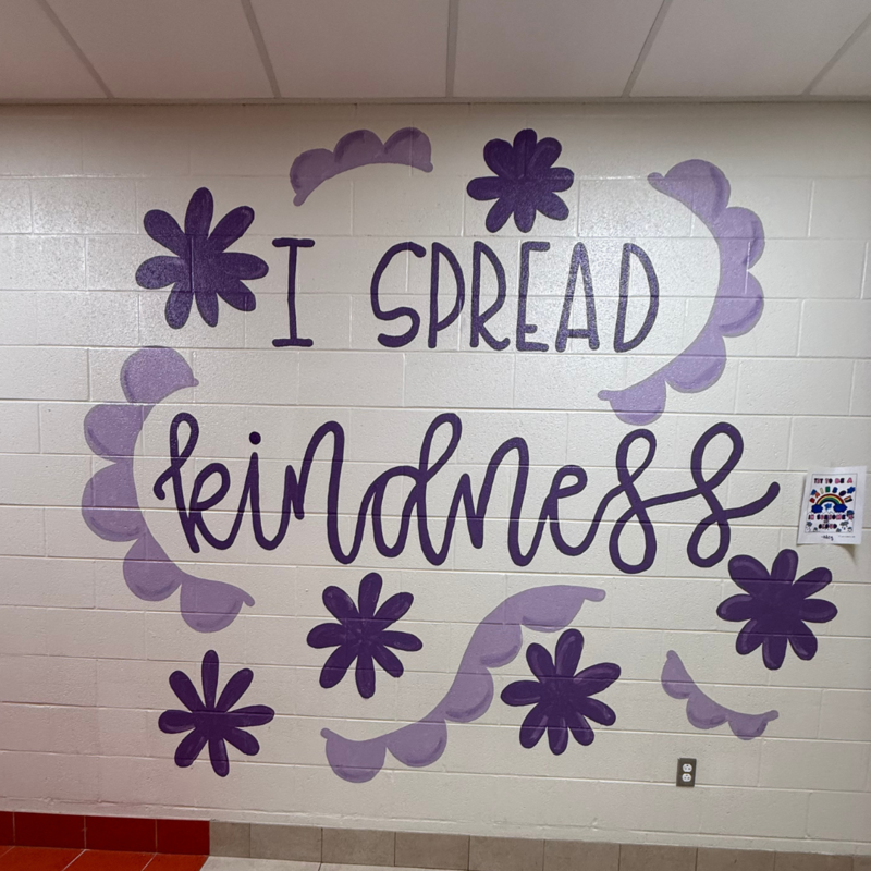 I spread kindness painted in purple on a white brick wall