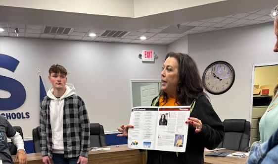 Tish holds a copy of her chambers magazine. Students are looking at her.