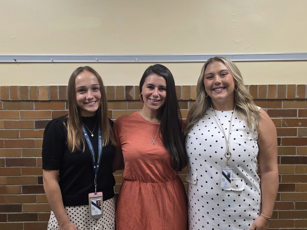 Three women pose for a photo in front of a brick wall, each wearing different tops.