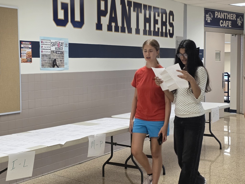 Two individuals read papers in a corridor with a "GU PANTHERS" sign and a "PANTNER CAFE" sign.