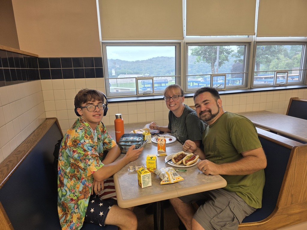 Three people in a booth at a restaurant, one wearing glasses, eating food with drinks nearby.