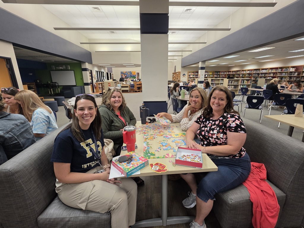 Four individuals sit around a table building a puzzle in a library.