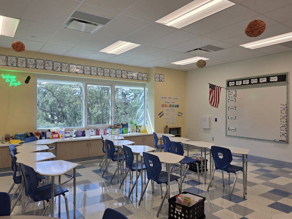 Classroom with desks and chairs arranged in rows. A whiteboard is on the wall, and a flag is displayed above it.