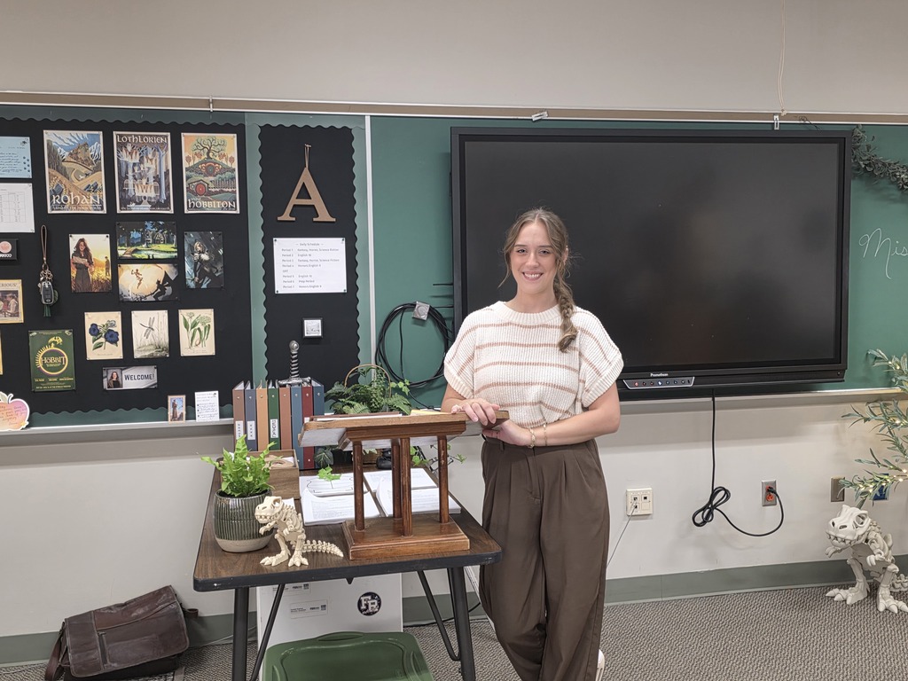 Woman in front of a classroom display. Table has a plant and dinosaur model.