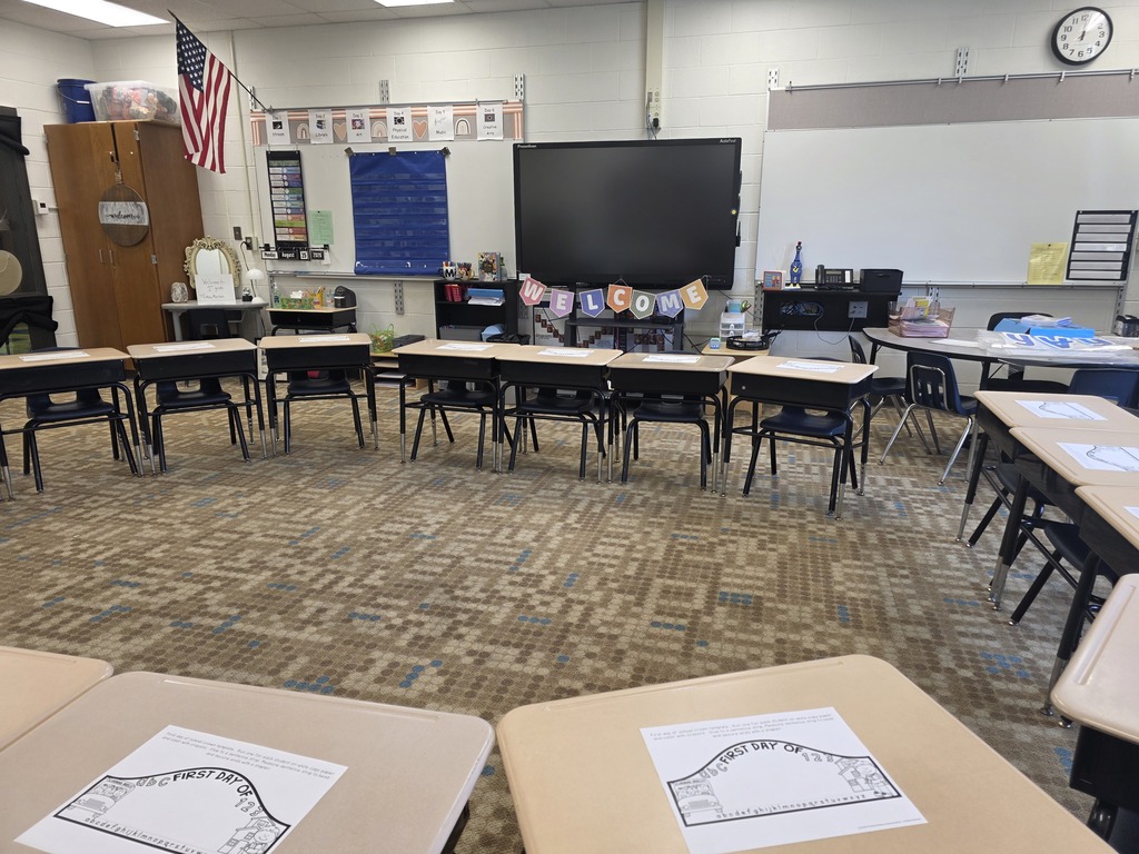 Empty classroom with desks and chairs arranged in a circle. A flat screen TV and a clock are on the wall.