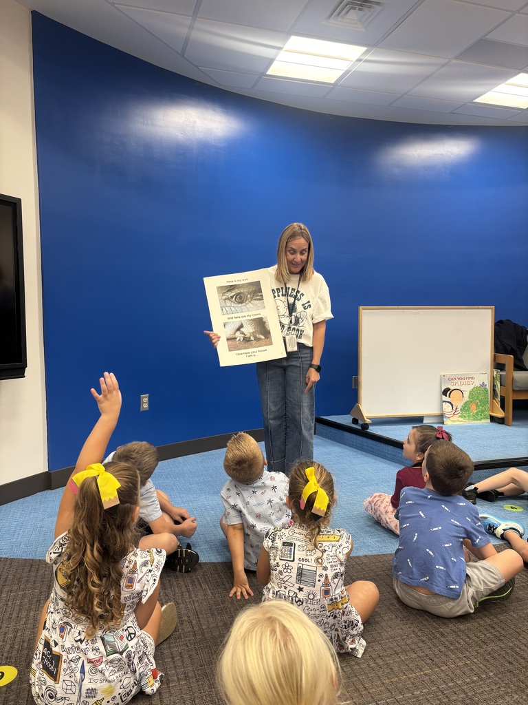 A woman holds a book while children sit on the floor in a room with blue walls.
