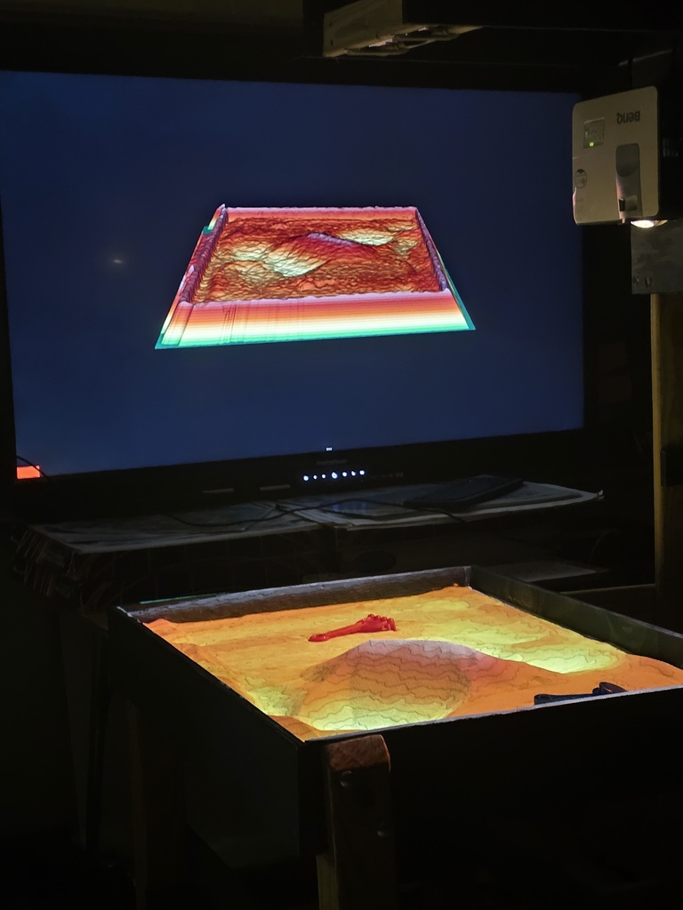 A large screen displays a red square map. Below, a touch-sensitive table shows a yellow map.