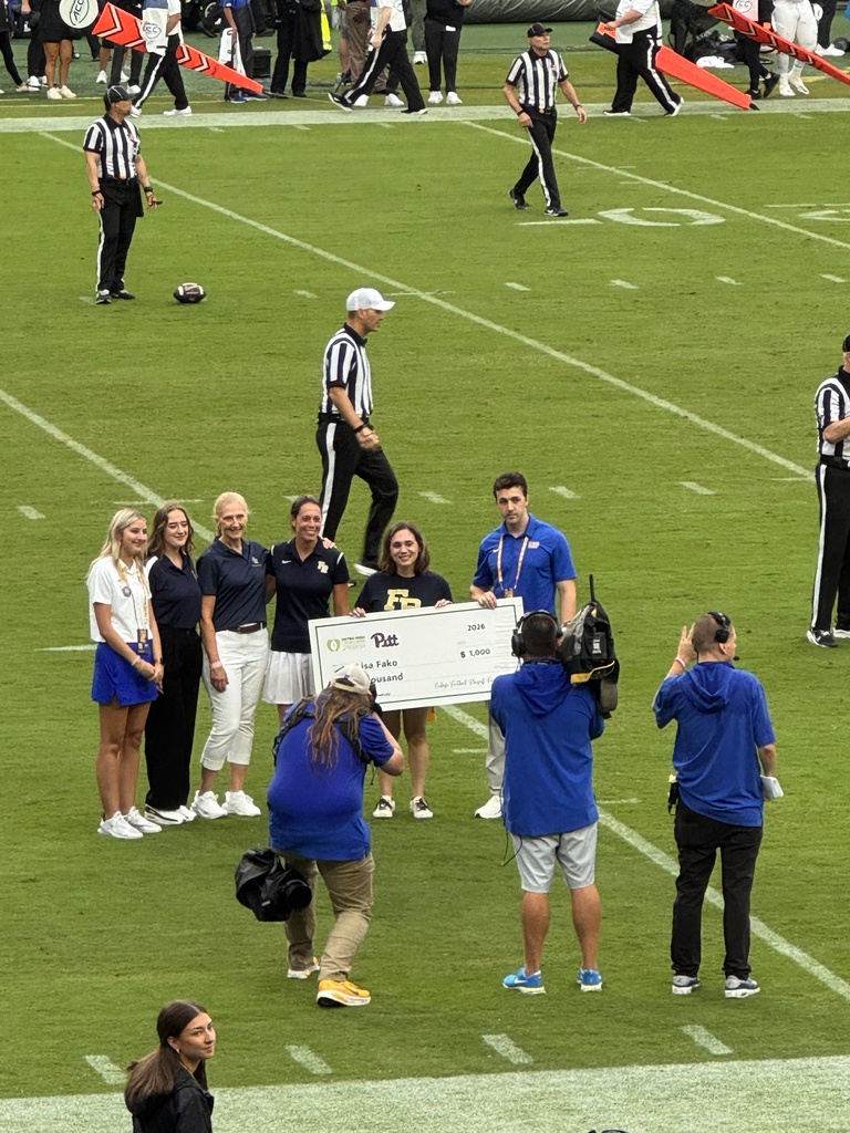 People on a football field, some holding a large check. A few officials are walking around.