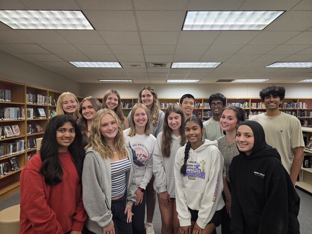 A group of people in a library with bookshelves in the background, standing together and smiling.