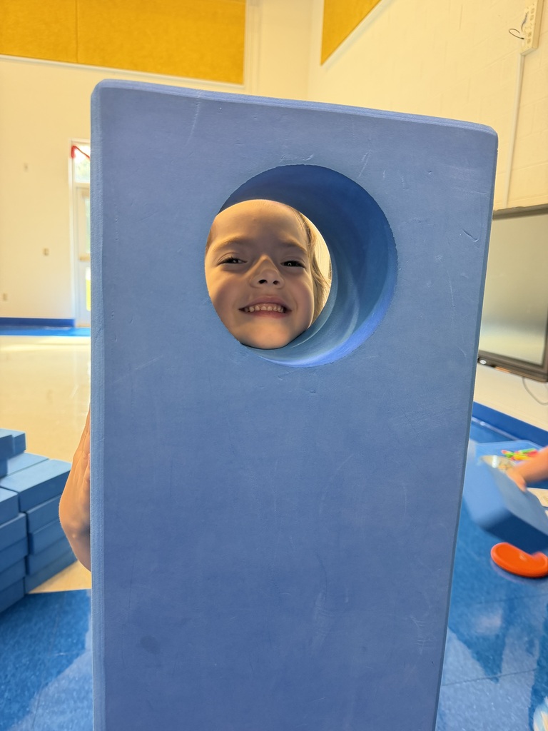 A young boy smiles and looks out from a circular opening in a blue structure.