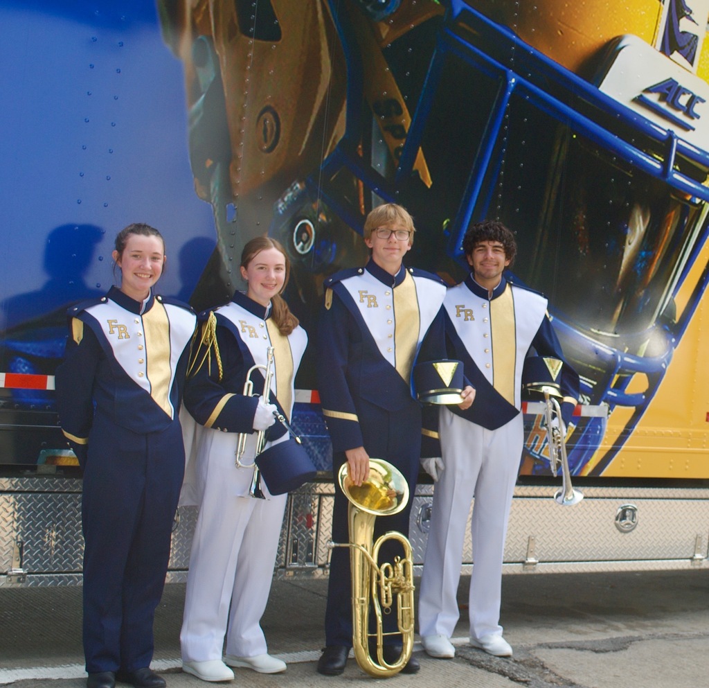 Four individuals in blue and white uniforms, each holding musical instruments, standing in front of a bus.