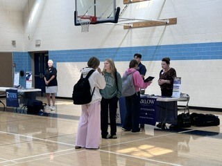 A basketball court with blue and white walls. A group of people are gathered around a table.