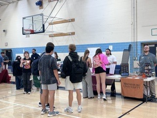 Several people stand in a gym with a basketball hoop in the background, near a table with items.