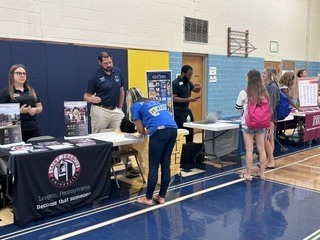 A group of people stands at tables in a gymnasium, some with laptops. A banner says "United Pennsylvania".