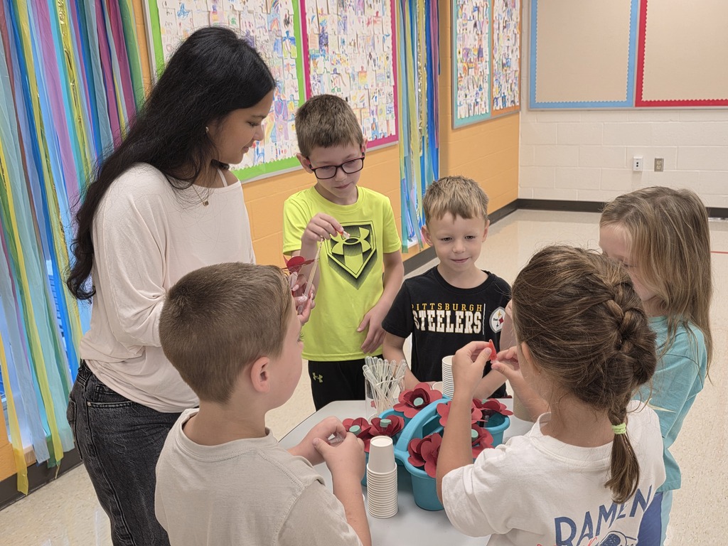 A woman and children gathered around a table with strawberries. Two children wear glasses. Bright decorations hang in the background.