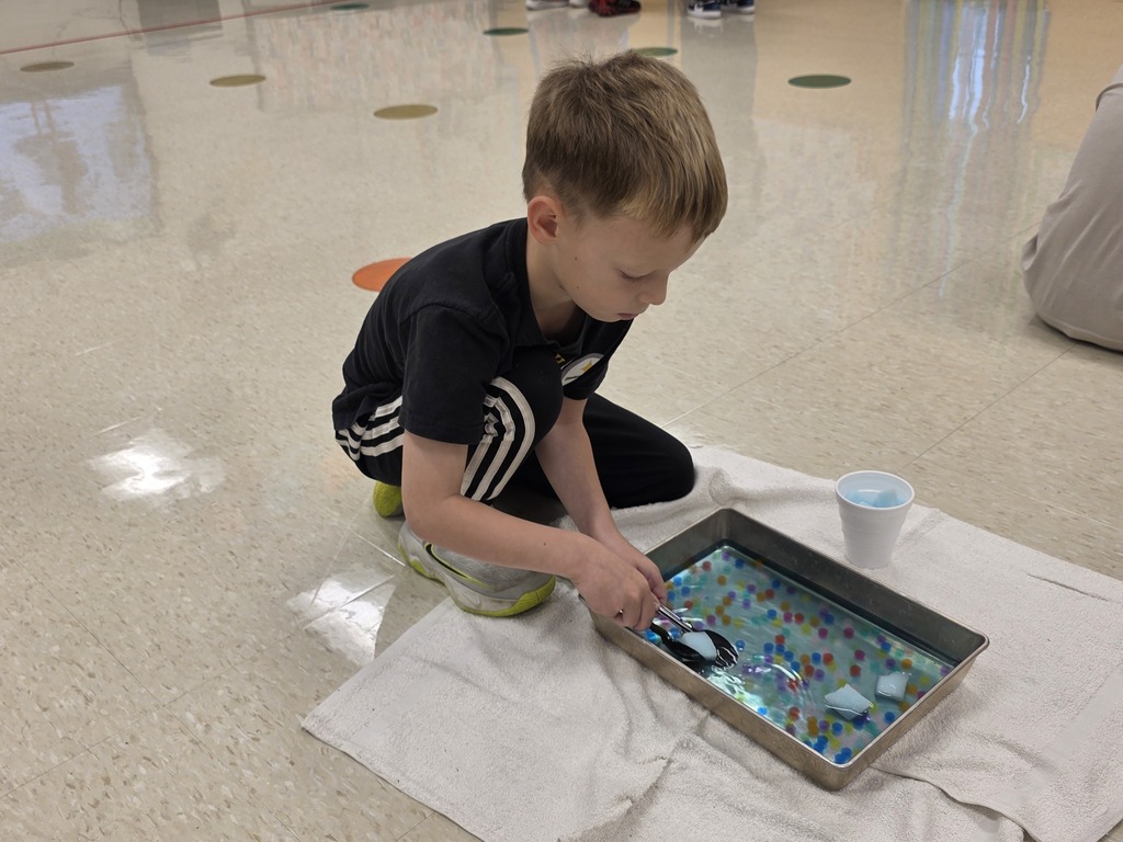 A child wearing a black t-shirt and black pants plays with a tray of sand on a white cloth.