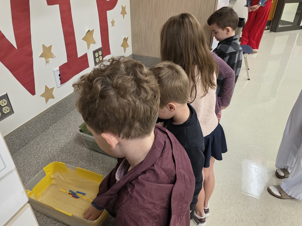 Several children are gathered around a yellow tray. They are looking at something inside it.