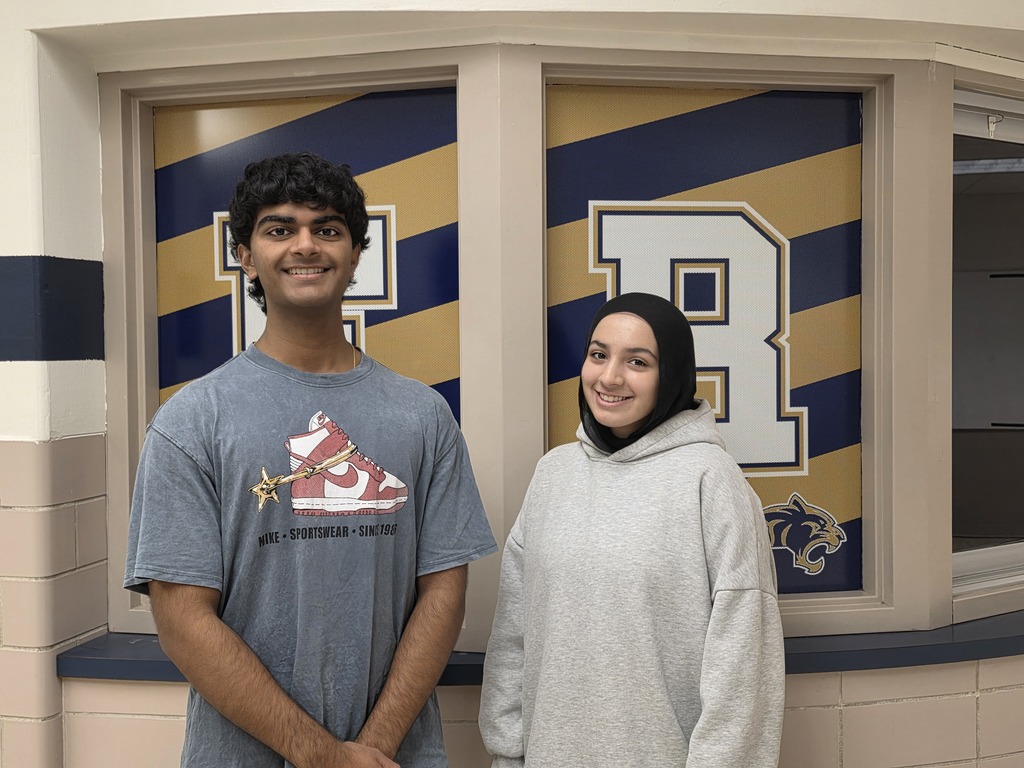 Two people standing in front of a window with a large R and a cat logo.