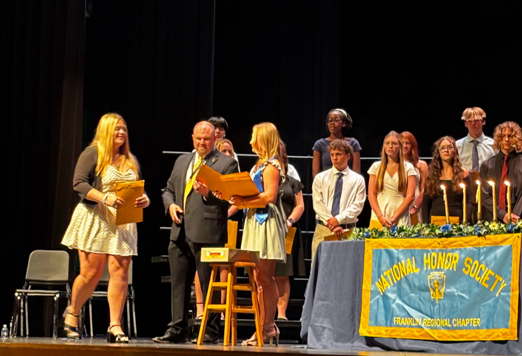 Group on stage for an induction ceremony. One person holds a candle, another holds a folder.