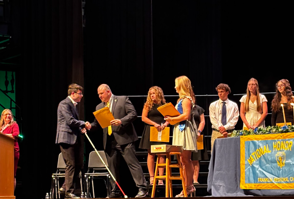 A group of people on a stage during an award ceremony. Some hold awards, and others stand behind a table.