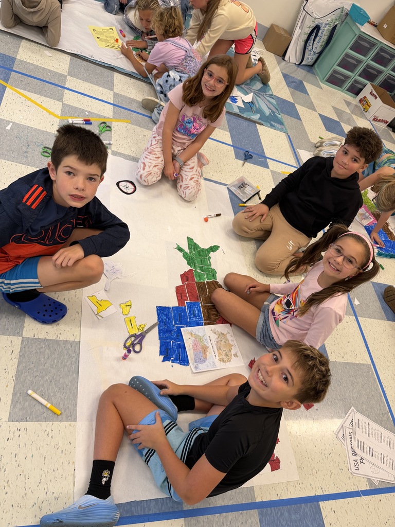 Group of children sitting in a circle on a floor with a checkered pattern. Some are working on art projects on paper.