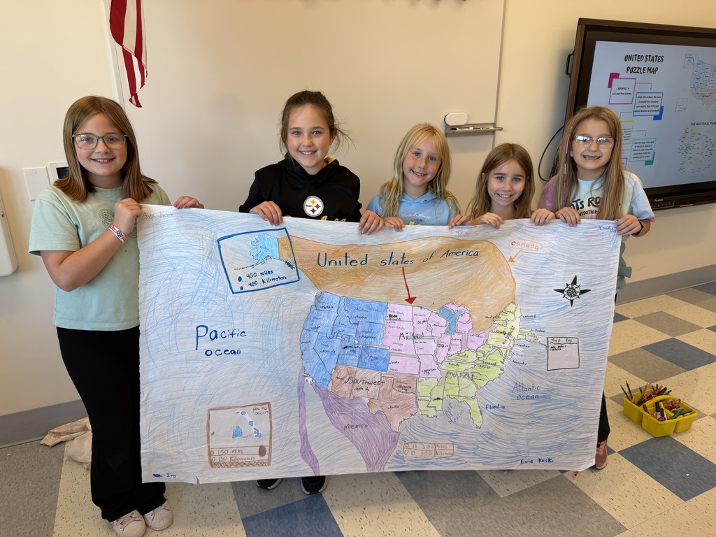 Five young girls display a handmade map of the United States. They stand in a classroom, wearing casual clothing.