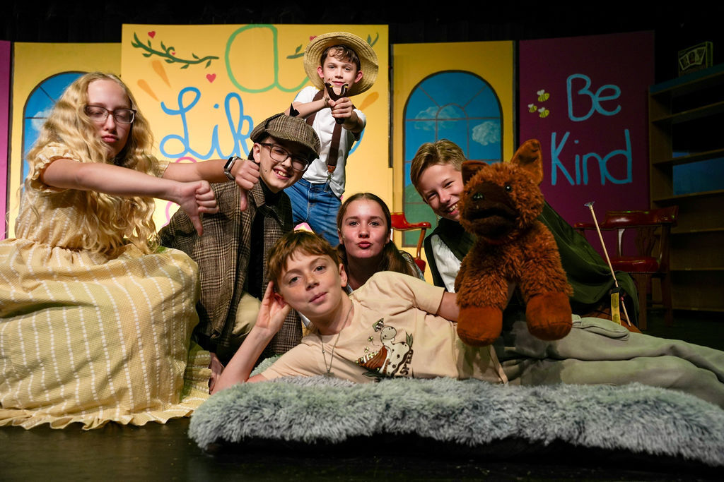 A group of children and adults on stage with backdrops reading "A Life" and "Be Kind."