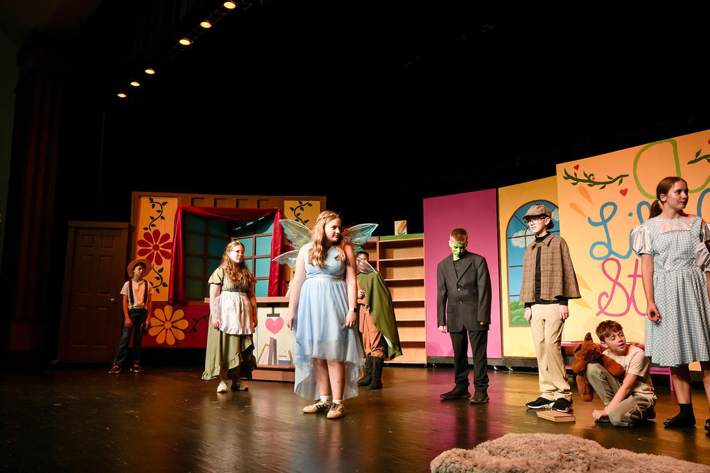 Group of children on stage in colorful costumes. A child crouches at the front.