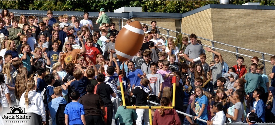 Stadium filled with spectators; large football above the crowd; many people cheering and standing on bleachers.