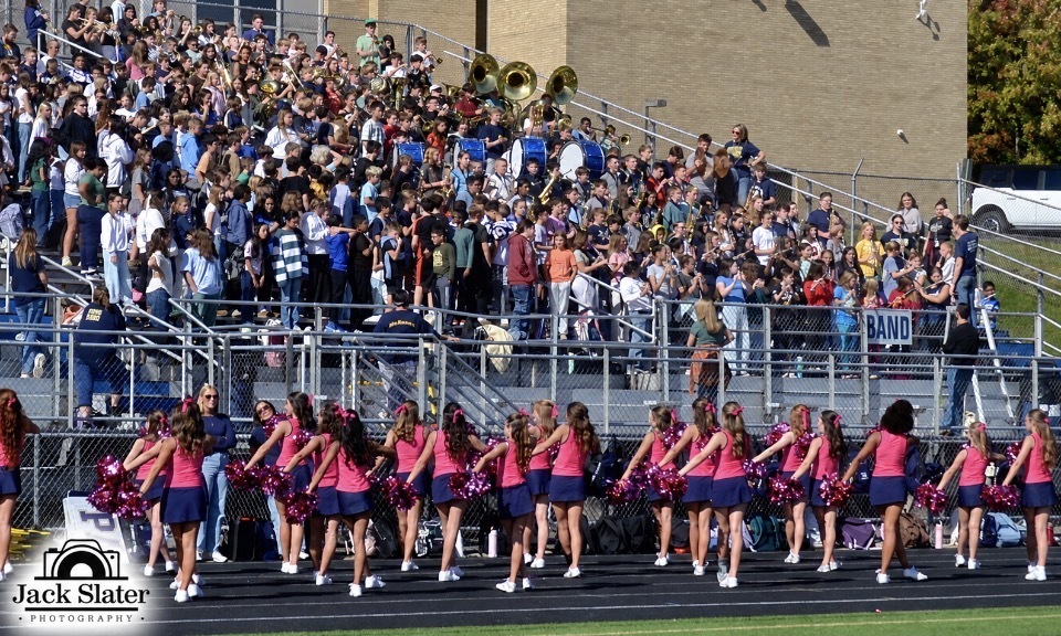 A cheerleading squad, wearing matching uniforms, performs on the field as a crowd watches from the stands.