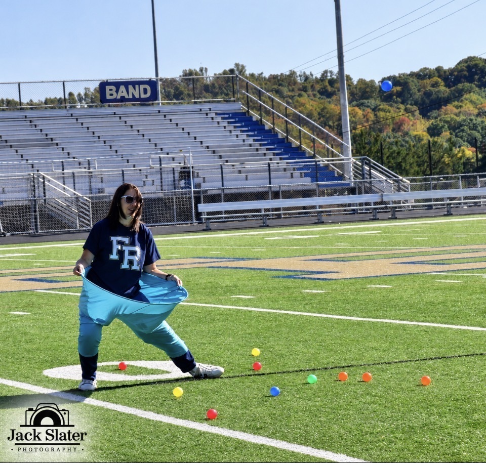 A person stands on a football field with a blue banner reading "FR" in the background.