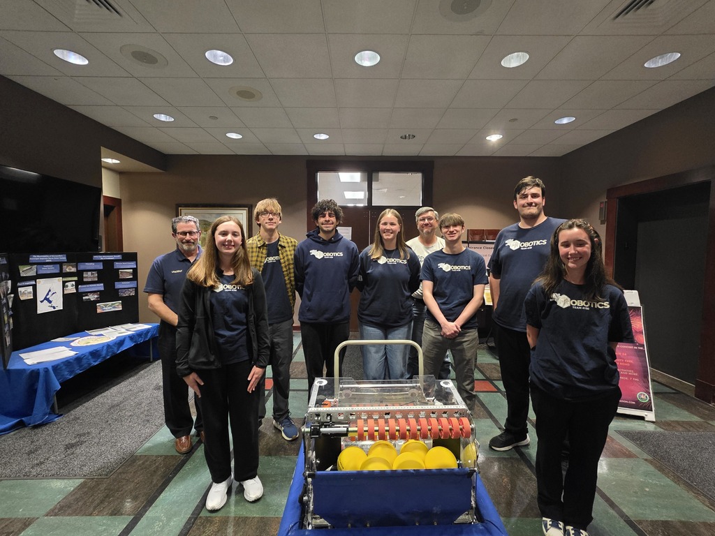 People in matching shirts, some standing near a machine with objects, others near a table.