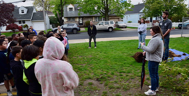 Students and teachers standing on grass outside.