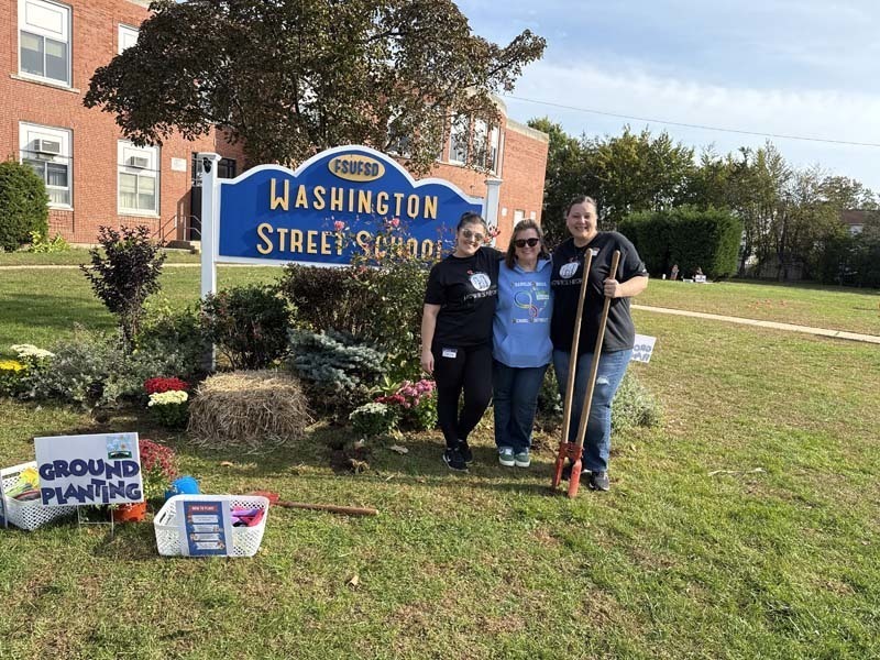 Students outside smiling at table.