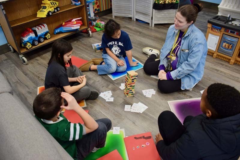 Students learning from teacher, sitting on floor.