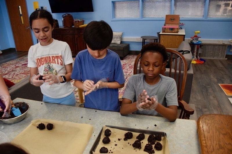 Children learning to mix soil for a gardening project with an instructor in a bright, inviting kitchen.
