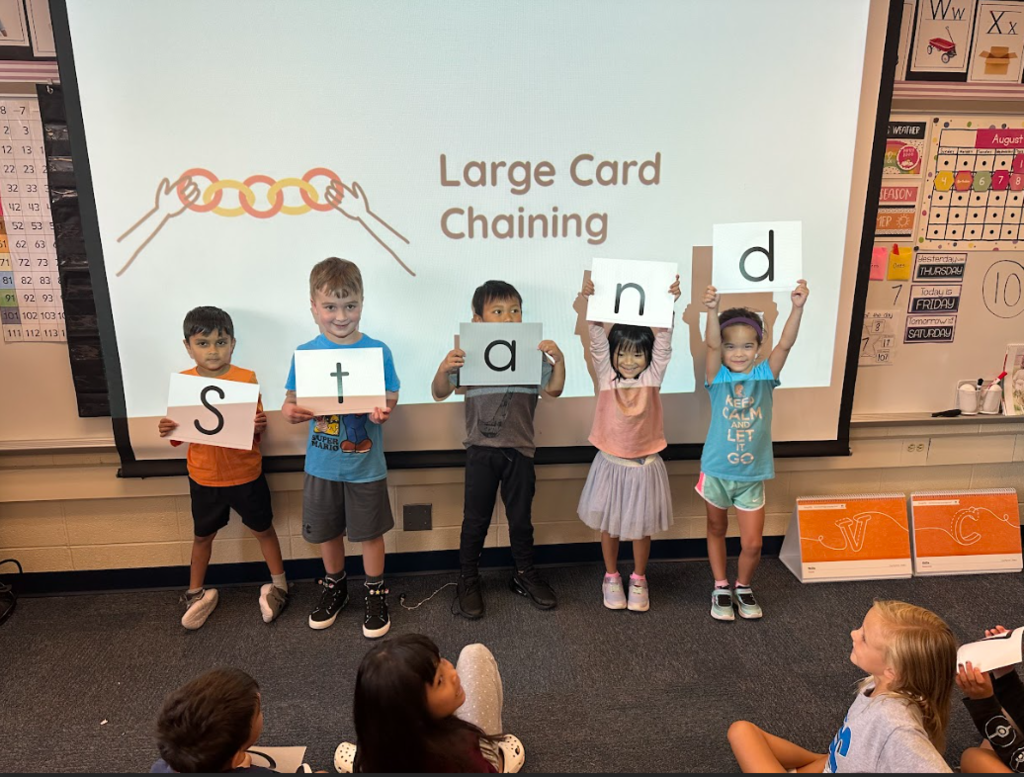 5 students holding leter signs to spell the word "Stand"