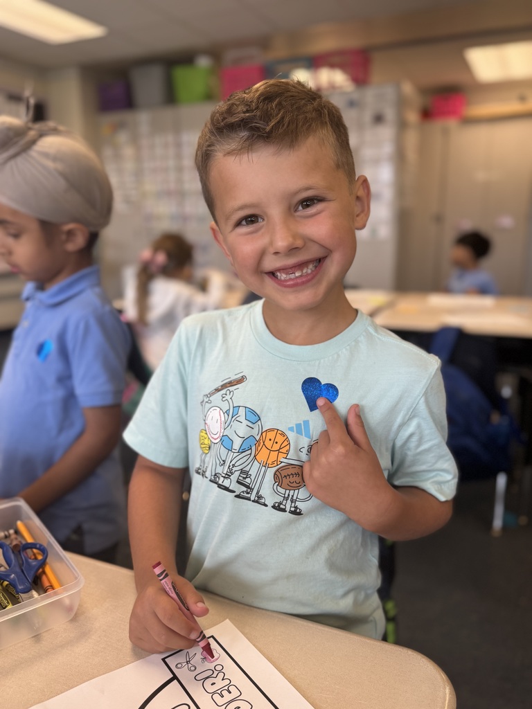 First grade student smiling and pointing to a blue heart sticker