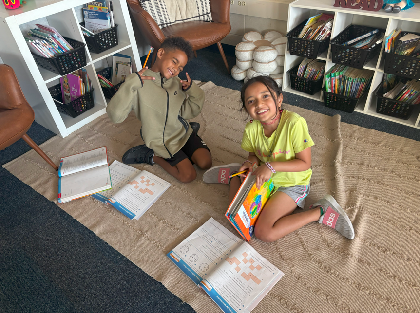 two students doing school work on the floor smiling