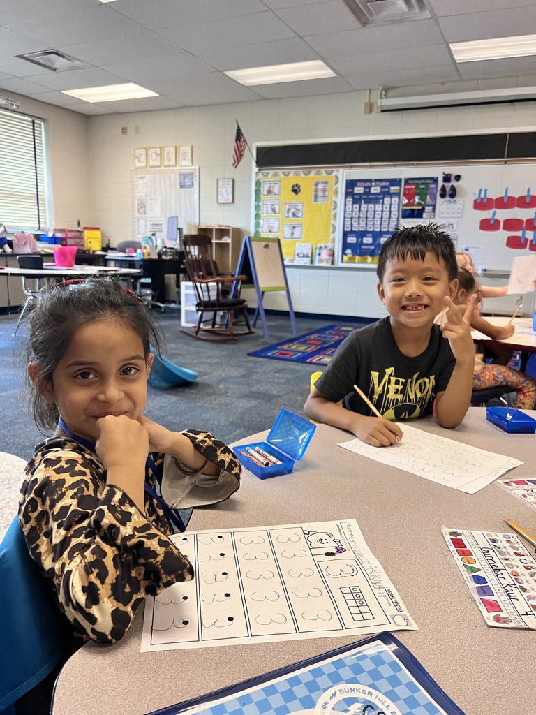 Two kindergarten students smiling while doing their classwork at the table