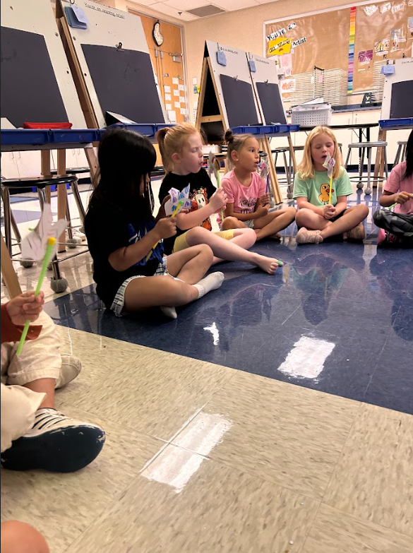 First grade students blowing on the pinwheels they made