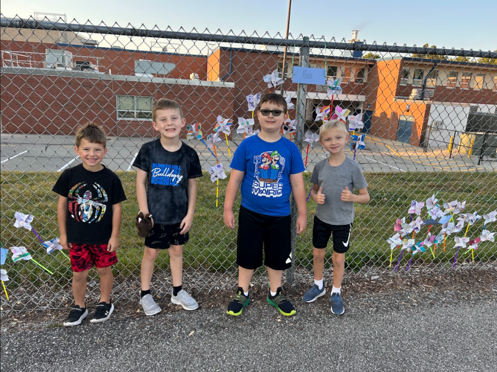 Students smiling in front of pinwheels in the fence