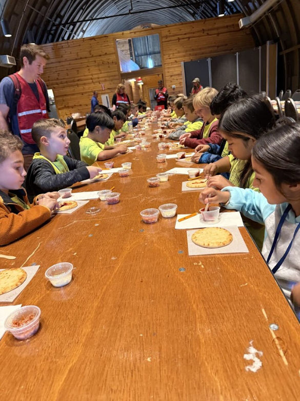 students sitting at table making mini pizzas