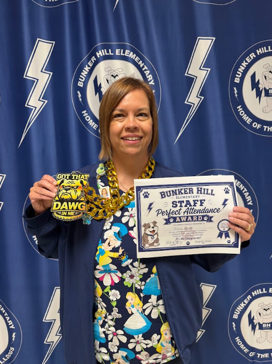 school nurse holding certificate and a gold necklace with big medallion celebrating perfect attendance