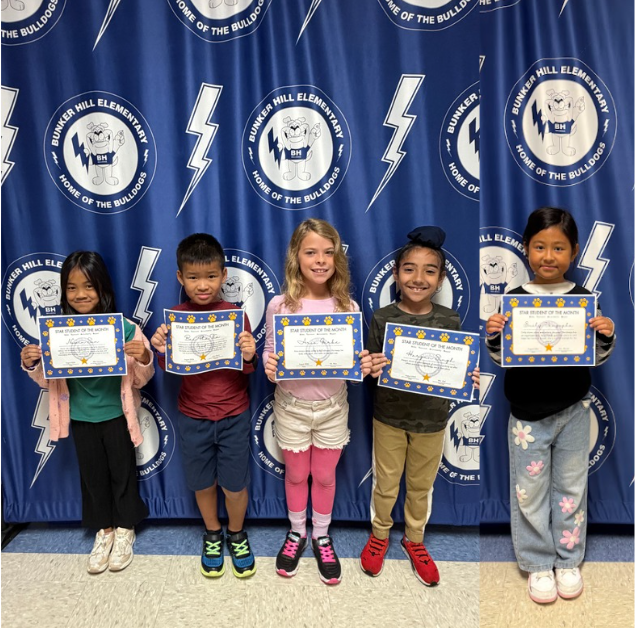 second grade students of the month standing in front of banner holding certificates smiling