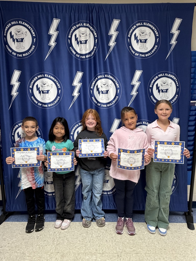 third grade students of the month standing in front of banner holding certificates smiling