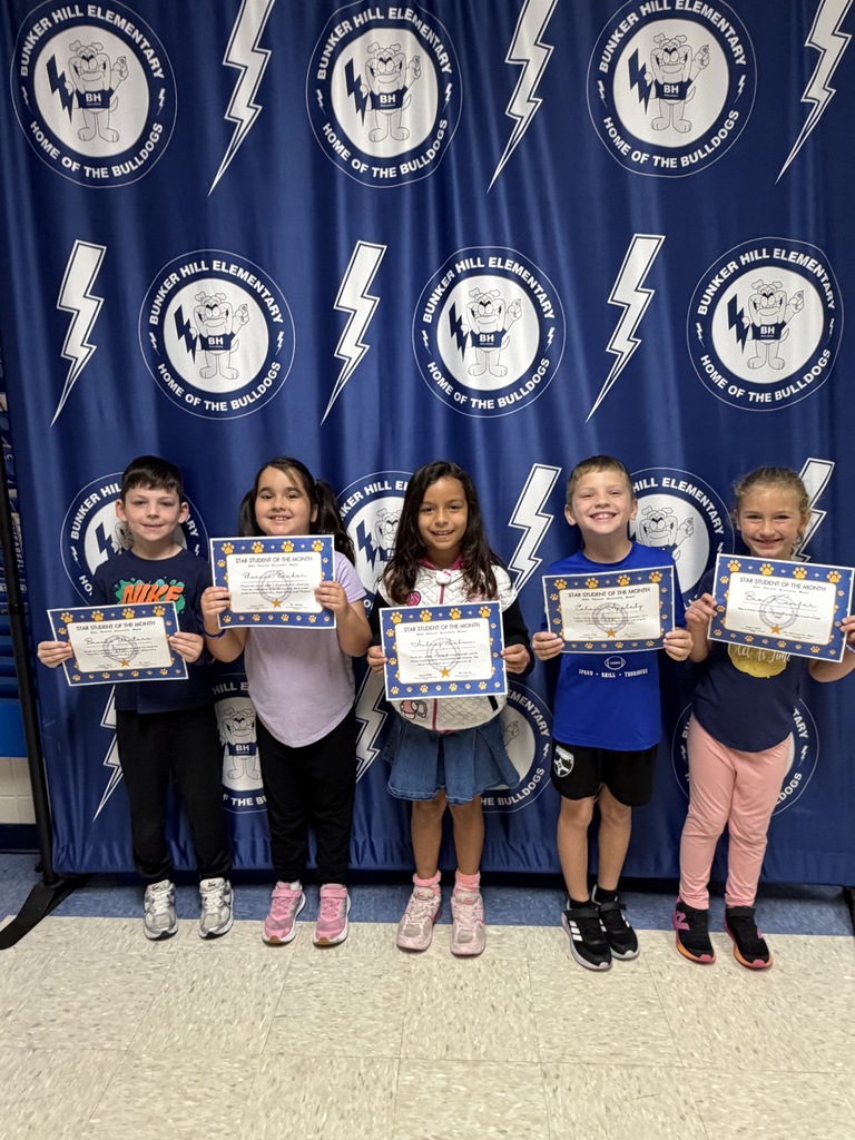first grade students of the month standing in front of banner holding certificates smiling