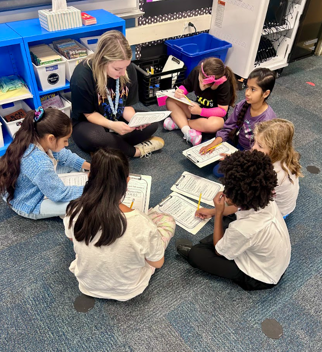 student sitting in a circle on the floor with a teacher doing a worksheet together