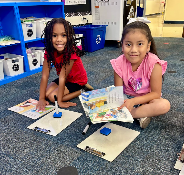 two students sitting on the floor with white board working together on reading